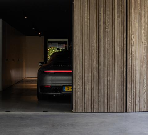 Moderne garage met afwerking in voorvergrijsd essen hout verticale profielen en beton vloer. 