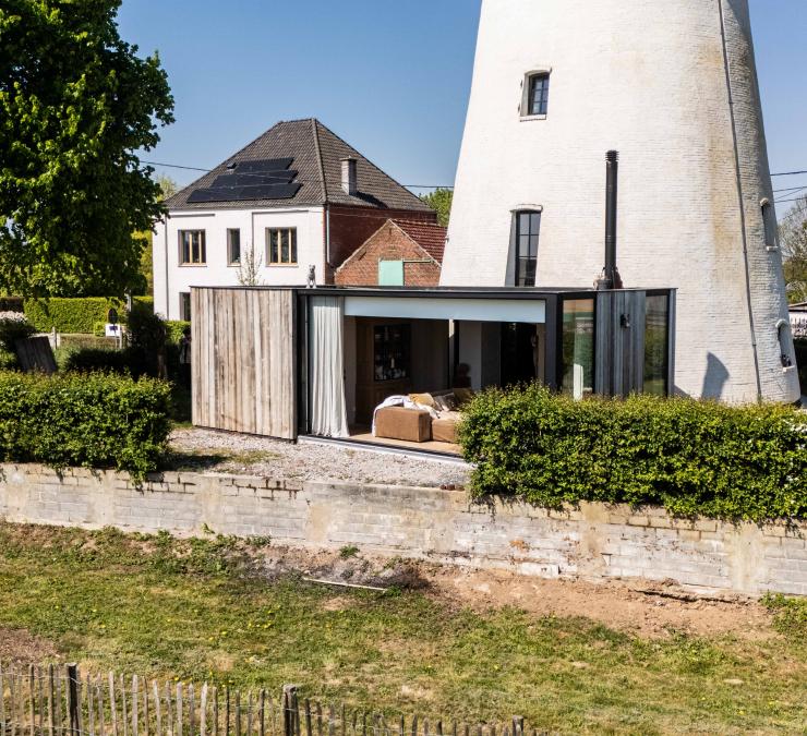 Aanbouw in barnwood met grote schuiframen bij witte molenwoning
